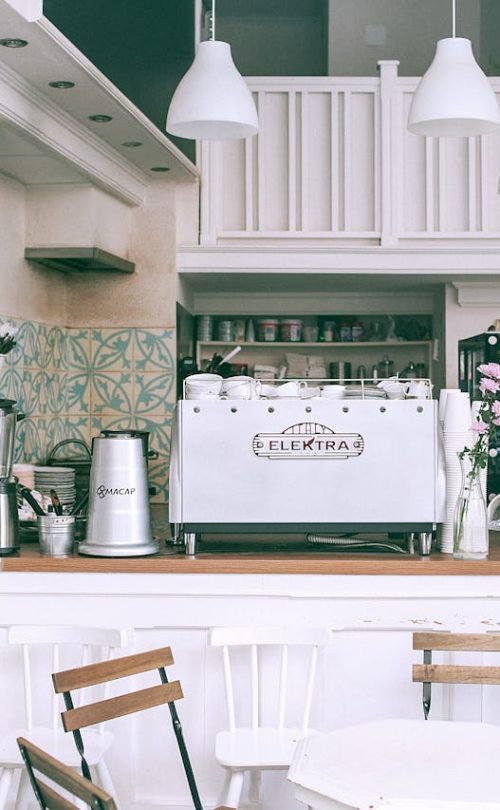 White kitchen set with coffee maker and appliances in small cozy coffee shop with flowers and table in daylight