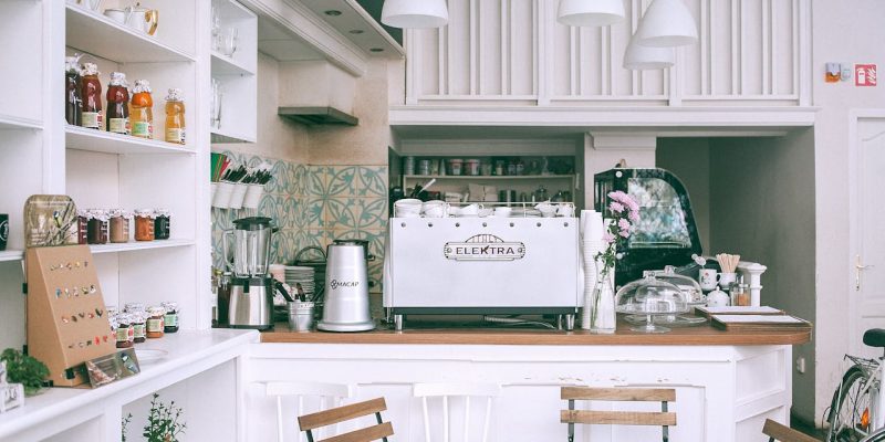 White kitchen set with coffee maker and appliances in small cozy coffee shop with flowers and table in daylight